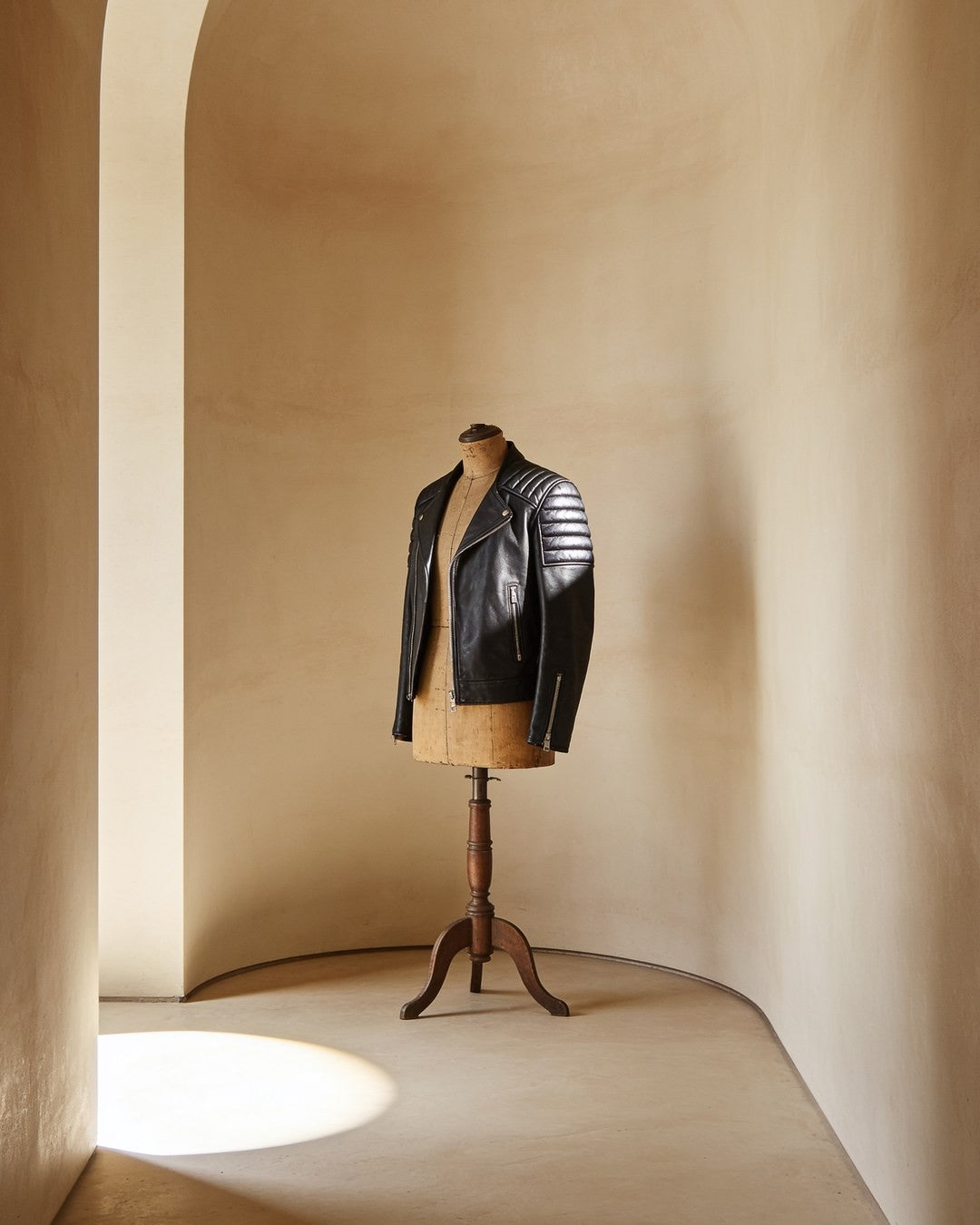 A black leather biker jacket with quilted shoulders on a wooden dress form in a sand-coloured plaster studio